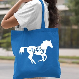 May include: A royal blue tote bag with a white silhouette of a horse and the name "Ashley" printed on it.
