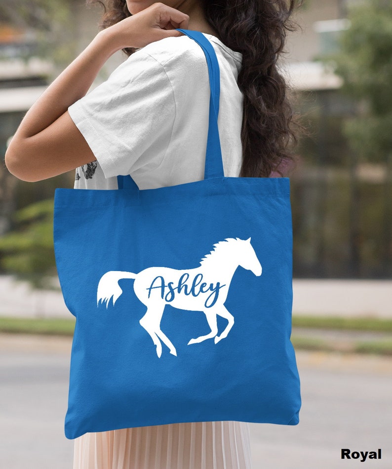 May include: A royal blue tote bag with a white silhouette of a horse and the name "Ashley" printed on it.