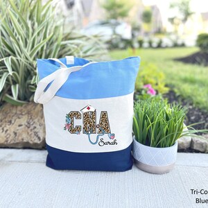 May include: A tri-color tote bag with a blue, white, and navy blue design. The bag features a leopard print design with the letters "CNA" and a stethoscope. The name "Sarah" is written below the design.