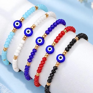 Puede incluir: Cinco pulseras de cuentas con cuentas facetadas en azul claro, blanco, azul oscuro, rojo y negro. Cada pulsera incluye un amuleto redondo de ojo turco con iris azul y cuentas espaciadoras doradas entre las cuentas de vidrio.