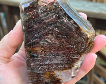 May include: A large, clear quartz crystal with brown, black, and pink inclusions. The crystal is faceted and has a rough, natural texture.