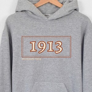 May include: A gray hooded sweatshirt with a brown rectangle containing the number "1913" and the text "Delta Sigma Theta" in a smaller font below.