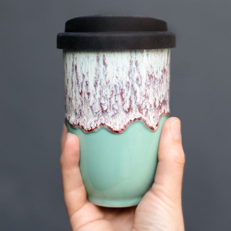 May include: A ceramic travel mug with a light green bottom and a white and red speckled top. The mug has a black silicone lid.