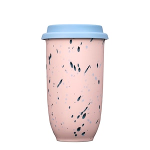 Könnte beinhalten: Ein zylindrischer Reisebecher mit hellrosa Basis und einem dunkelblauen Sprenkelmuster auf der Außenseite. Der Becher ist mit einem abnehmbaren hellblauen Deckel versehen, der eine flache Oberseite und einen etwas breiteren Rand aufweist.