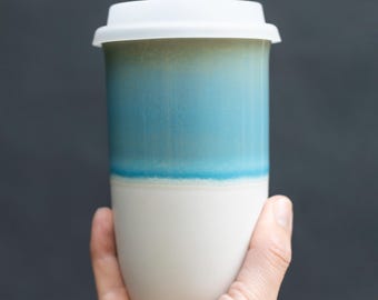 May include: A white ceramic travel mug with a blue and white glaze. The mug has a white lid.