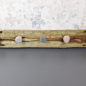 May include: A rustic wooden branch with five smooth stones attached as hooks. The branch is weathered and has a natural, organic look.