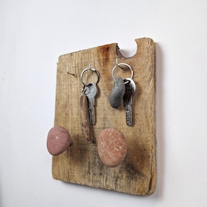 Peut inclure: Un porte-clés en bois rustique avec deux boutons ronds en pierre et trois crochets. Le porte-clés a une finition en bois naturel et est décoré de deux petites pierres.