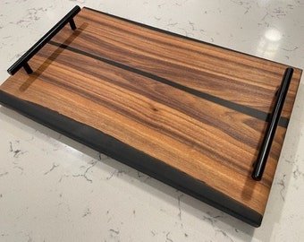 May include: A wooden serving tray with black epoxy resin accents and black metal handles. The tray is made of wood with a natural grain pattern.