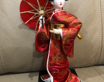 Traditional Japanese Geisha doll with glass eyes and red and gold Kimono dress with umbrella. New in box