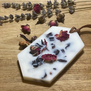 May include: A white hexagonal wax melt with dried rose petals and other botanicals. The wax melt is on a wooden surface with dried lavender sprigs.