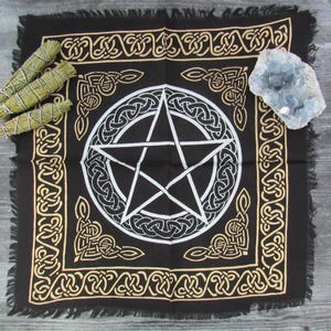 Puede incluir: Tela de altar negra con un pentagrama blanco rodeado por un borde de nudo celta dorado. La tela tiene un borde con flecos.