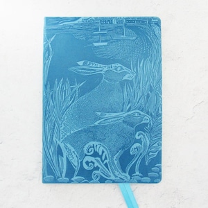 May include: A teal blue leather journal with an embossed design of two hares in a field of tall grass. The journal has a ribbon bookmark.