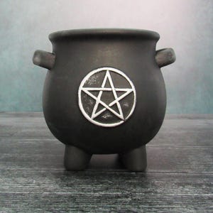 Peut inclure: Chaudron noir avec un pentagramme argenté. Le chaudron a trois pieds et deux poignées.