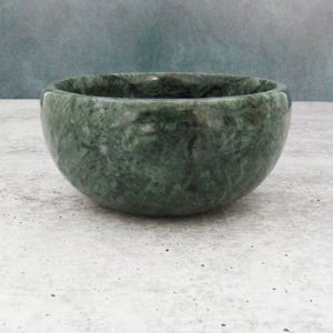 May include: A green marble bowl with a swirling pattern. The bowl is round and has a smooth, polished surface.