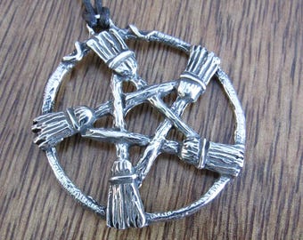 May include: Silver-toned pendant featuring a pentagram design with five brooms arranged within a circle. The brooms are intricately detailed, and the pendant hangs from a black cord. The pendant is displayed on a wooden surface.