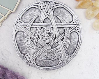 Puede incluir: Un objeto decorativo circular plateado con un diseño de pentagrama con nudos celtas y detalles de luna creciente. El artículo tiene un aspecto envejecido y probablemente está hecho de metal. El diseño está en relieve.