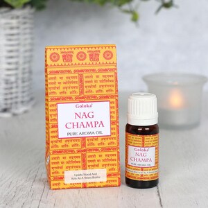 K&ouml;nnte beinhalten: Eine gelbe Schachtel mit Sanskrit-Text und den Worten "Goloka Nag Champa Pure Aroma Oil" darauf. Eine kleine braune Glasflasche mit wei&szlig;em Verschluss und dem gleichen Text auf dem Etikett. Die Flasche steht auf einer hellen Holzoberfl&auml;che.
