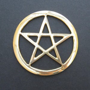 May include: A gold-coloured metal pentagram charm with a circular border. The pentagram is a five-pointed star with a point facing upwards.