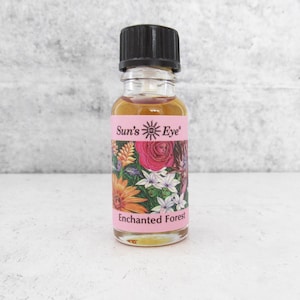 Puede incluir: Una pequeña botella de vidrio de aceite esencial con una tapa negra. La etiqueta es rosa con un diseño floral y el texto "Sun's Eye Enchanted Forest".