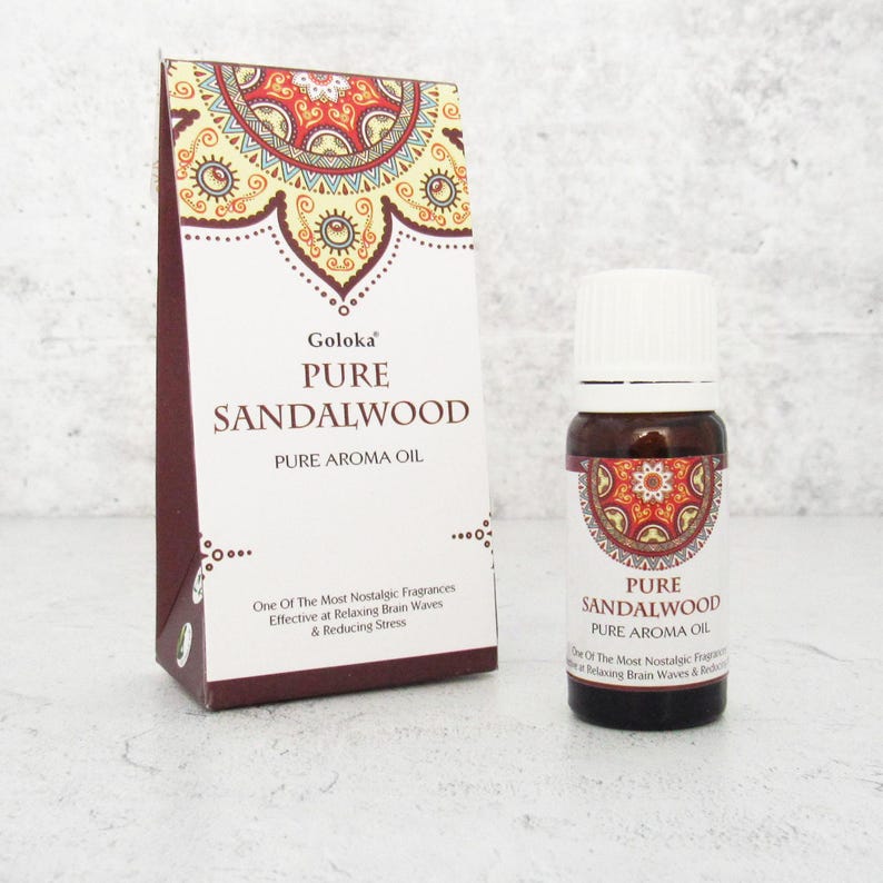 K&ouml;nnte beinhalten: Eine kleine braune Glasflasche mit wei&szlig;em Verschluss, die reines Sandelholz-&Auml;therisches &Ouml;l enth&auml;lt. Die Flasche ist mit "Goloka Pure Sandalwood Pure Aroma Oil" beschriftet. Das Etikett zeigt ein rotes, gelbes und wei&szlig;es Mandala-Design. Die Flasche steht auf einer wei&szlig;en Oberfl&auml;che.