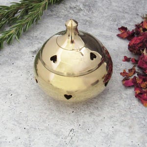 May include: A gold metal incense burner with a round shape and a domed lid. The burner has heart-shaped cutouts around the sides.