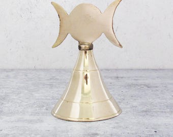 May include: A gold-colored brass bell with a triple moon design on the top. The bell is a traditional style with a rounded bottom and a flared top.