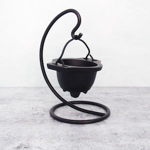 May include: Black metal incense burner with a hanging cauldron and a curved stand. The cauldron has a small lip around the top and three small feet.