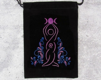 Puede incluir: Bolsa de terciopelo negro con un diseño bordado en rosa de una mujer sosteniendo una luna con tres lunas crecientes sobre su cabeza. La mujer está rodeada de diseños florales azules y rosas.