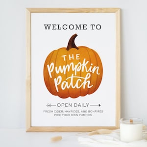 Könnte beinhalten: Ein gerahmtes Schild mit dem Text "Willkommen im The Pumpkin Patch" und einer Illustration eines orangefarbenen Kürbisses. Das Schild sagt auch "Täglich geöffnet" und listet Aktivitäten wie frischen Apfelsaft, Heufahrten und Lagerfeuer auf.