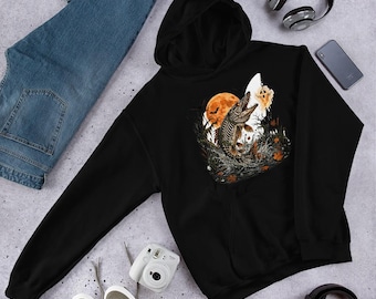 Può includere: Una felpa nera con cappuccio caratterizzata da una stampa grafica di un pesce scheletrico che salta fuori dall'acqua davanti a una grande luna arancione. Il design include sagome scure di alberi, pipistrelli in volo e un piccolo fantasma.
