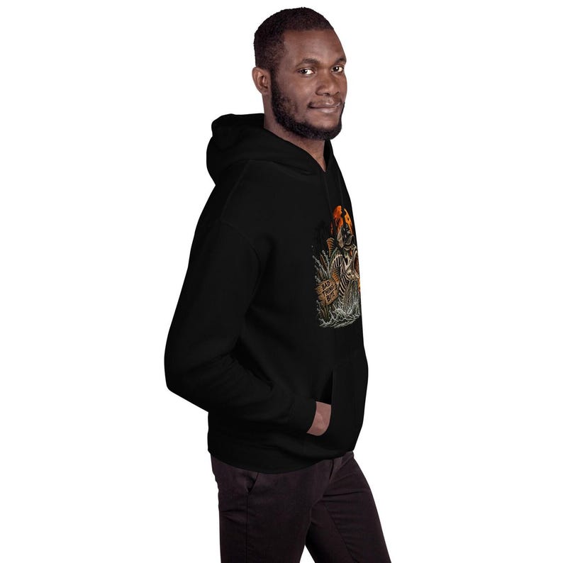 K&ouml;nnte beinhalten: Ein schwarzer Kapuzenpullover mit einem Grafikdruck eines skelettierten Fisches, der vor einem orangefarbenen Mond aus dem Wasser springt. Das Design zeigt Schilf und ein kleines Holzschild mit dem Text "BAD FISHING DAY" in einem dunklen Stil.