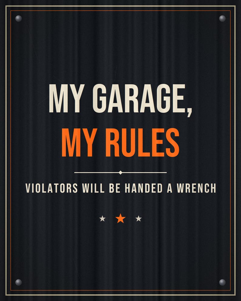 Pu&ograve; includere: Una targa rettangolare in metallo nero con una texture ondulata e un bordo sottile. Il testo recita MY GARAGE, MY RULES in bianco e arancione, seguito da VIOLATORS WILL BE HANDED A WRENCH in bianco. Tre piccole stelle sono centrate in basso.