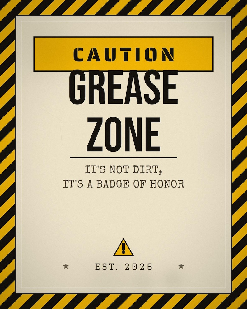 Pu&ograve; includere: Un cartello rettangolare con un bordo a strisce diagonali gialle e nere. Il testo recita CAUTION GREASE ZONE, IT'S NOT DIRT, IT'S A BADGE OF HONOR e EST. 2026. Un triangolo giallo con un punto esclamativo &egrave; centrato sopra l'anno.