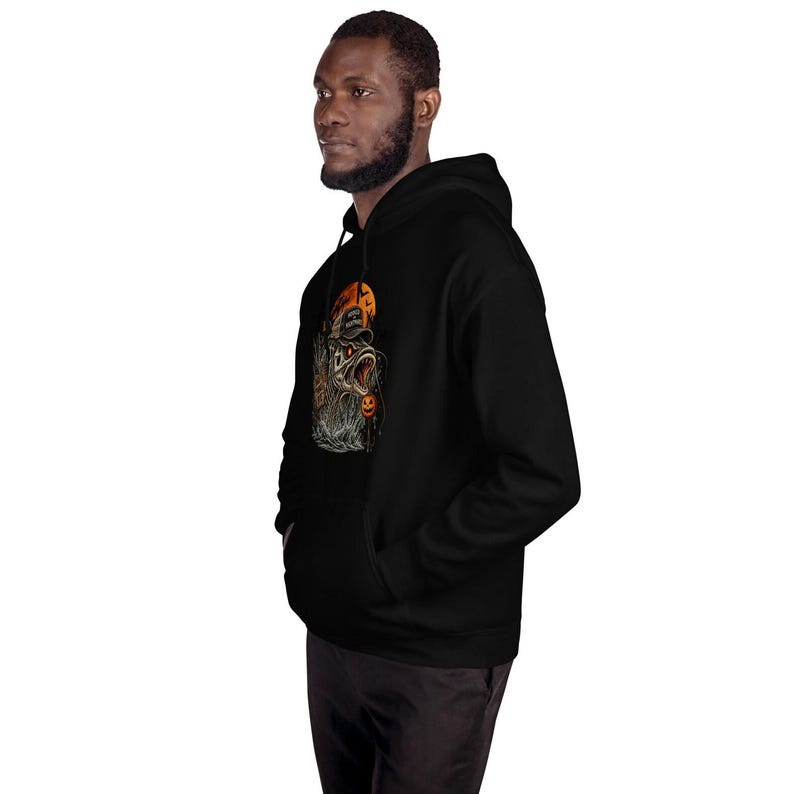 K&ouml;nnte beinhalten: Ein schwarzer Kapuzenpullover mit einem Grafikdruck eines Fisches, der eine Baseballkappe mit dem Text "HOOKED HALLOWEEN" vor einem orangefarbenen Mond tr&auml;gt, erg&auml;nzt durch einen kleinen K&uuml;rbis und Flederm&auml;use im Detail.