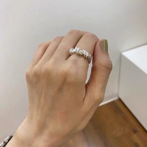 May include: A silver ring with a twisted design. The ring is worn on a person's finger.