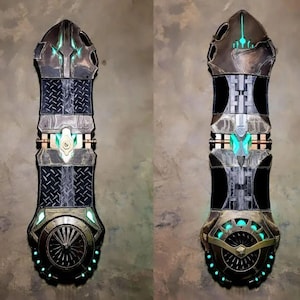 May include: Two decorative skateboard decks with a futuristic design. The decks are made of wood and painted in a dark gray, black, and gold color scheme. The decks have a detailed design with intricate patterns and glowing green lights.