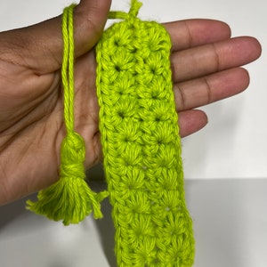 May include: A lime green crocheted bookmark with a tassel. The bookmark is made with a simple stitch pattern and has a long, thin shape.