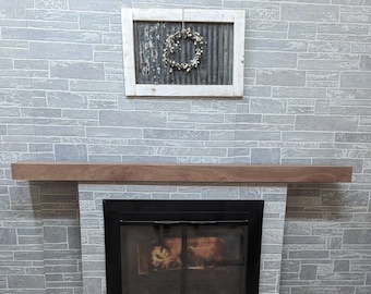 May include: A fireplace with a wooden mantel and a black metal firebox. The fireplace is surrounded by gray brick wallpaper. A white framed picture with a metal wreath hangs above the mantel.