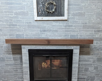 May include: A wooden mantel shelf above a black fireplace with a glass door. The fireplace is set against a gray brick wall.