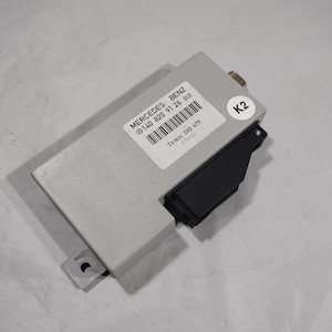 May include: A gray electronic control unit with a label that reads "MERCEDES BENZ 0 140 820 91 26 1021" and "TEMIC 3X0 479 97846". The unit has a black connector and a label with the letter "K2" on it.