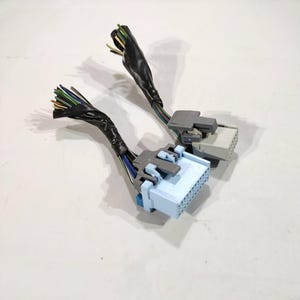 May include: Two electrical connectors with multiple colored wires. The connectors are light blue and gray, with a series of pins. The wires are wrapped in black tape.