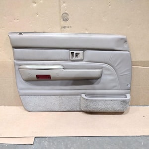Op de afbeelding: Beige auto deurpaneel met een gewatteerd bovendeel, een rechthoekige handgreep en een onderste deel met een stoffen zak. Voorzien van een rode reflector en bevestigingspunten. Het paneel is beige.