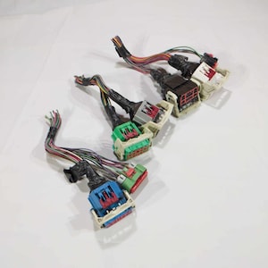 Pode incluir: Vários conectores elétricos multicoloridos com feixes de fios. Os conectores são em várias cores, incluindo azul, verde e branco, com detalhes em vermelho e preto. Os fios são de várias cores.