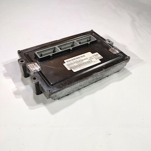 May include: A rectangular, black electronic control module with three gray connectors. A white label with barcodes and text is affixed to the top. The module has a metallic, textured frame and is set against a white background.