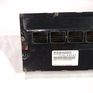 May include: A black electronic control module with multiple connector ports. A white label displays the text "DAIMLERCHRYSLER" and "440AE". The module has a rectangular shape and is secured with screws.