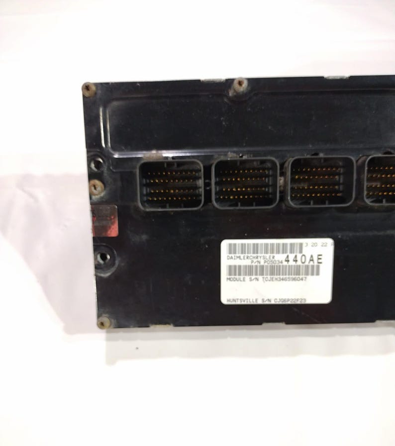 May include: A black electronic control module with multiple connector ports. A white label displays the text "DAIMLERCHRYSLER" and "440AE". The module has a rectangular shape and is secured with screws.