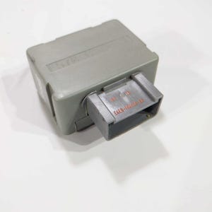 Op de afbeelding: Een grijze elektrische component voor auto's met een rechthoekige behuizing en een rechthoekige connector. De connector heeft de tekst "E6EB-14A604-AA" erop gedrukt. De component staat op een witte achtergrond.