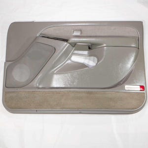 Puede incluir: Panel de puerta de coche gris con altavoz, manija y sección de tela beige. El panel tiene un acabado liso y brillante con un acento rojo y blanco. Esta pieza de automóvil está diseñada para el interior de un vehículo.