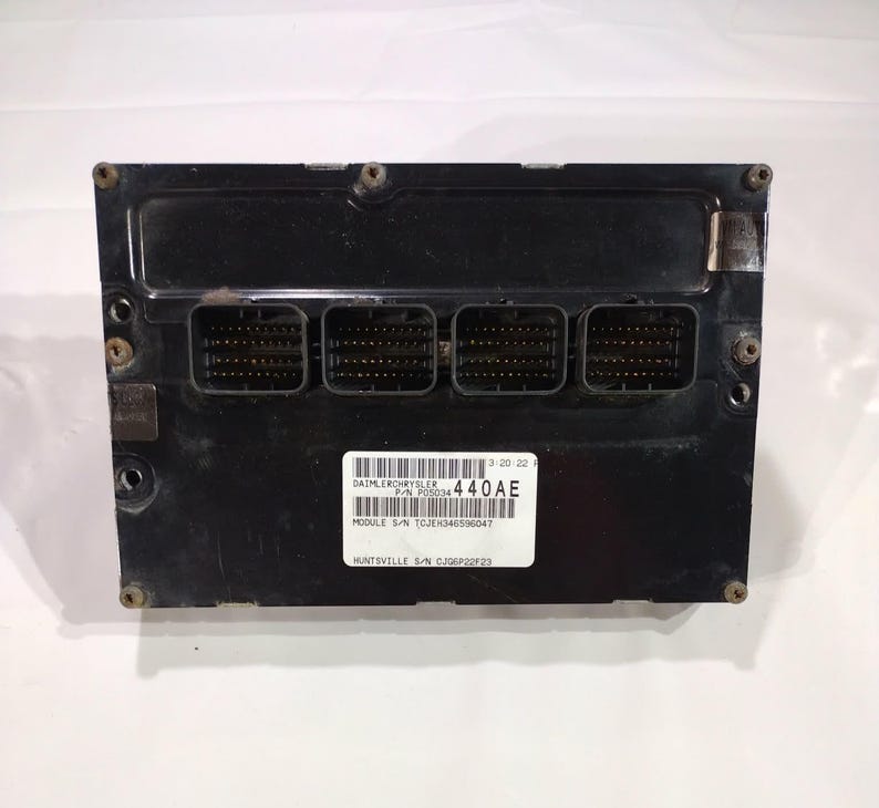 May include: A black electronic control module with multiple connector ports. A white label displays text including "DAIMLERCHRYSLER" and "440AE". The module has several screw holes and is likely for automotive use.