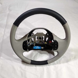 May include: A grey and black leather steering wheel with a perforated design and stitching. The steering wheel has controls for audio and cruise control.